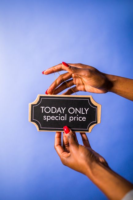 A person's hands, with red-painted nails, are holding a small rectangular sign with a decorative border that reads 'TODAY ONLY special price' against a plain blue background. One hand is gripping the